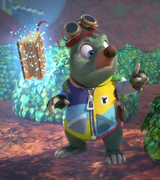 Dotty, mit einem Fernglas vor den Augen, sitzt getarnt in einem Busch und beobachtet etwas in der Ferne. Moley und das magische Buch Mauli befinden sich neben ihr.