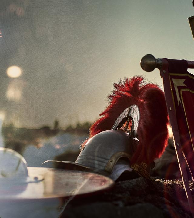 Collage: Links ein römischer Soldat, rechts eine römische Standarte und ein Helm auf einer Mauer.