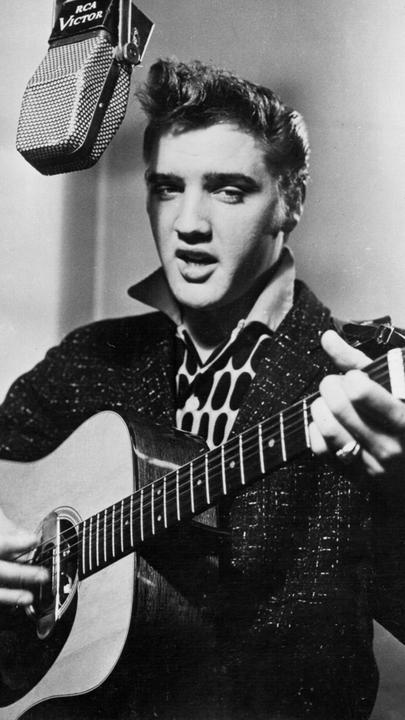 "Die sieben Leben des Elvis Presley": Schwarz-Weiß-Foto: Elvis Presley singt in ein Studiomikrofon und spielt dabei Gitarre.