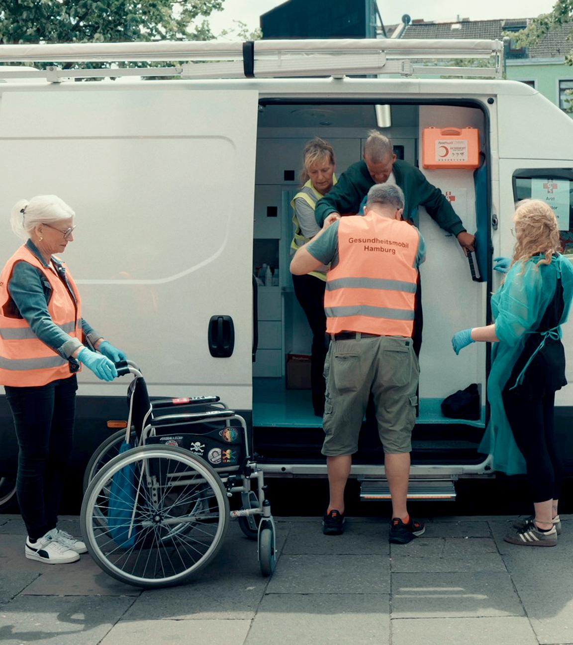 Menschen ohne Krankenversicherung fallen im Gesundheitssystem häufig durchs Raster – wie hier in Hamburg finden sie medizinische Hilfe in Gesundheitsmobilen. "Die Spur: Todkrank auf der Straße": Mehrere Personen stehen um das Gesundheitsmobil herum. 