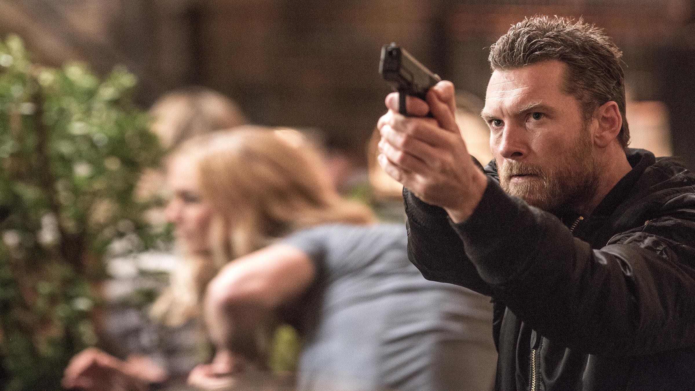 Stephen Lucas (Sam Worthington) steht mit gezogener Waffe in einer Menschenmenge.