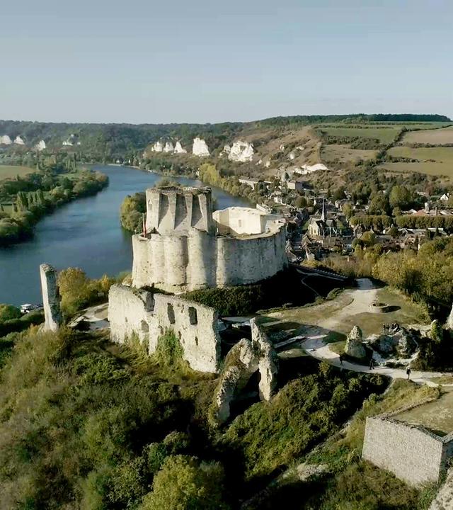 "Die Superburg des Richard Löwenherz": Luftaufnahme einer Schlossruine auf einem Hügel, umgeben von mehreren Mauern, Bäumen und einem Fluss.
