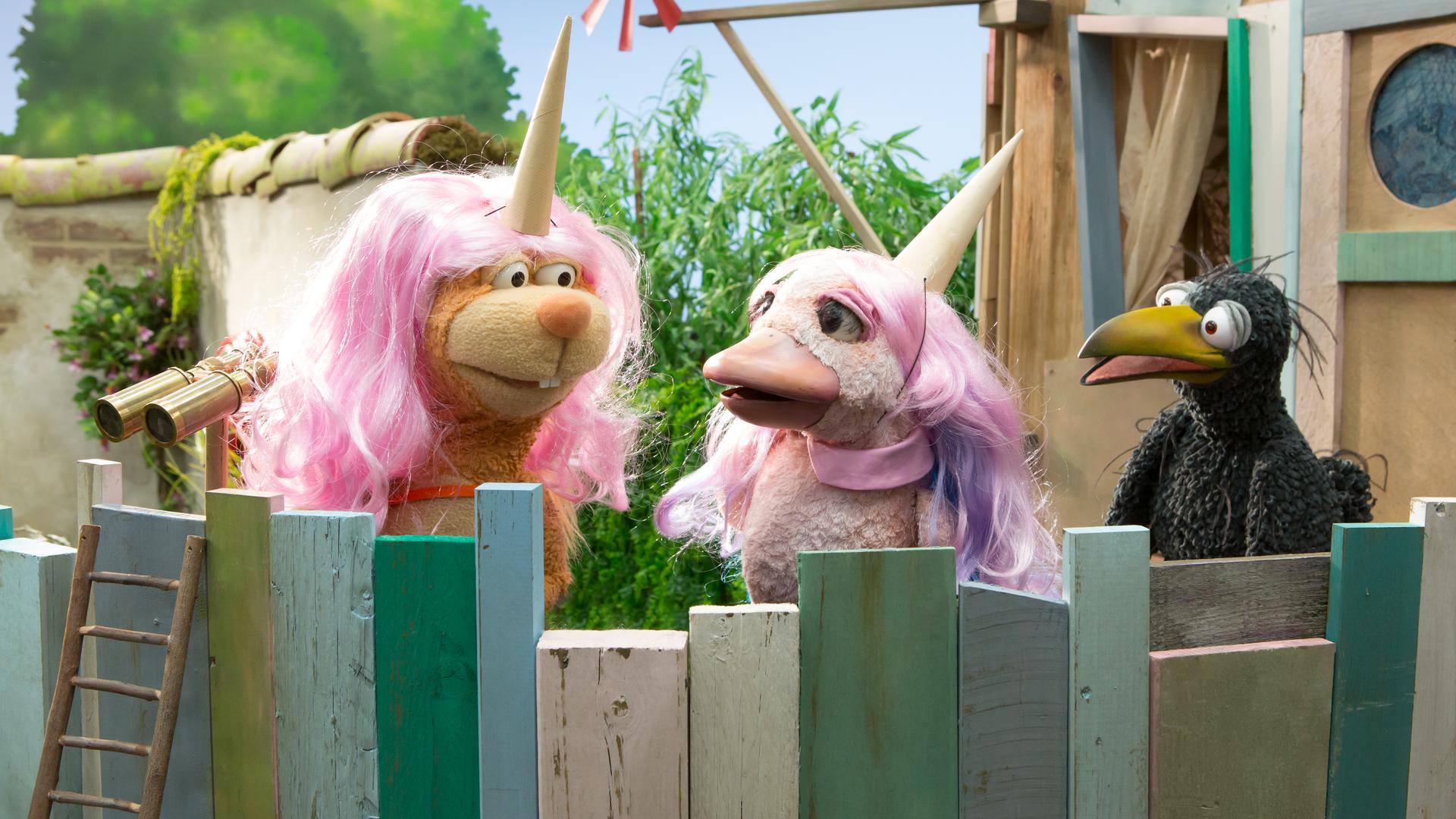 Rabe Rudi ist auf der Baumhaus-Plattform und schaut entsetzt auf Eichhörnchen Ella und Lina. Die beiden tragen rosa Perücken und Einhorn-Hörner auf den Köpfen und scheinen Rudi nicht zu bemerken.