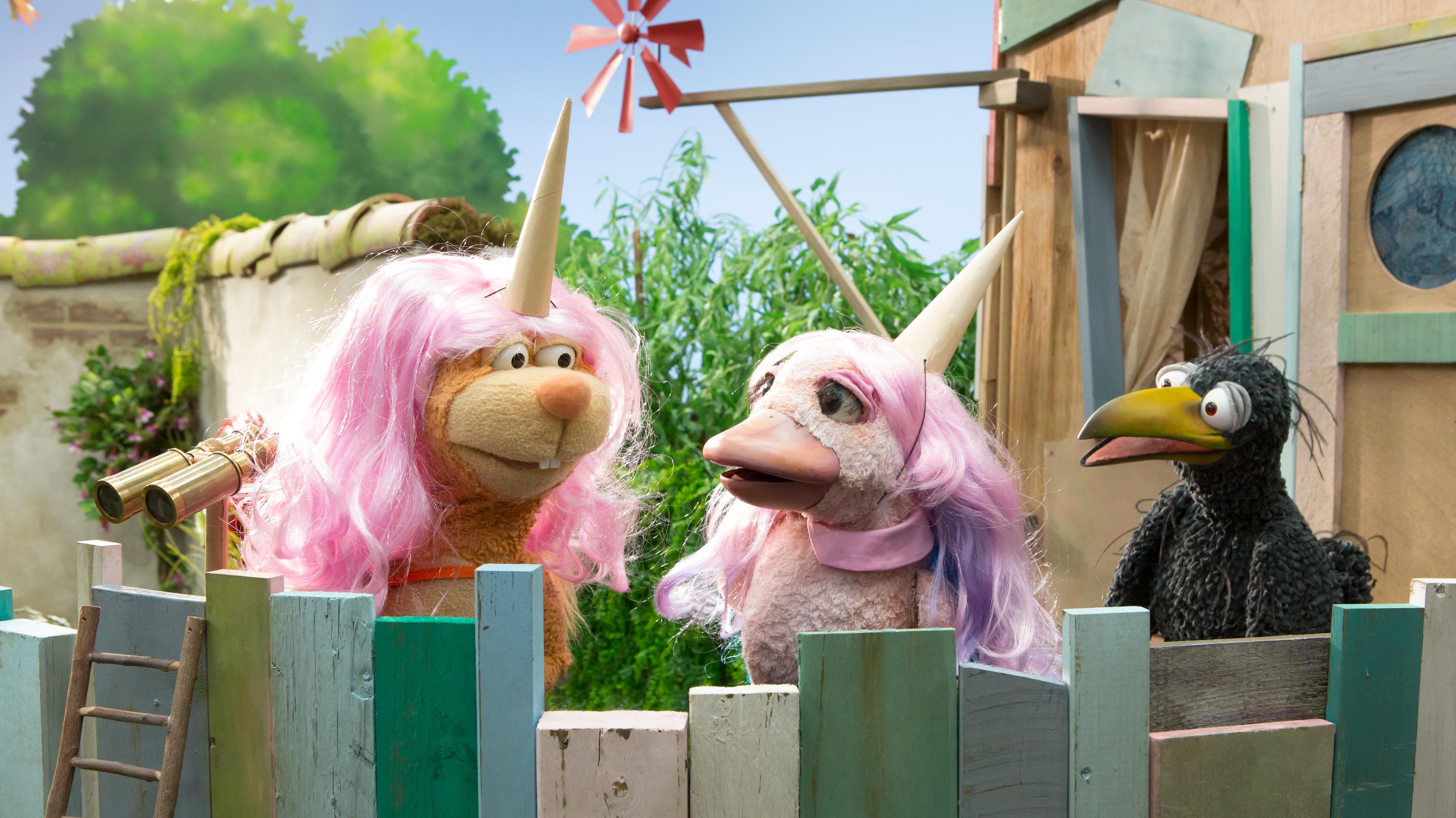 Rabe Rudi ist auf der Baumhaus-Plattform und schaut entsetzt auf Eichhörnchen Ella und Lina. Die beiden tragen rosa Perücken und Einhorn-Hörner auf den Köpfen und scheinen Rudi nicht zu bemerken.