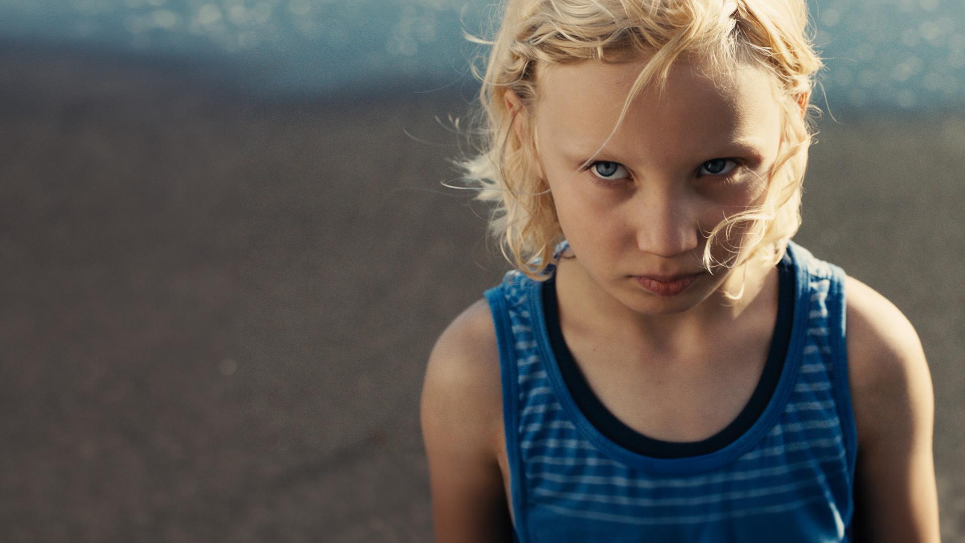 "Die Tochter":  Luca (Helena Zengel) in einem ärmellosen T-Shirt steht am Strand und schaut mit ernstem Blick nach oben.