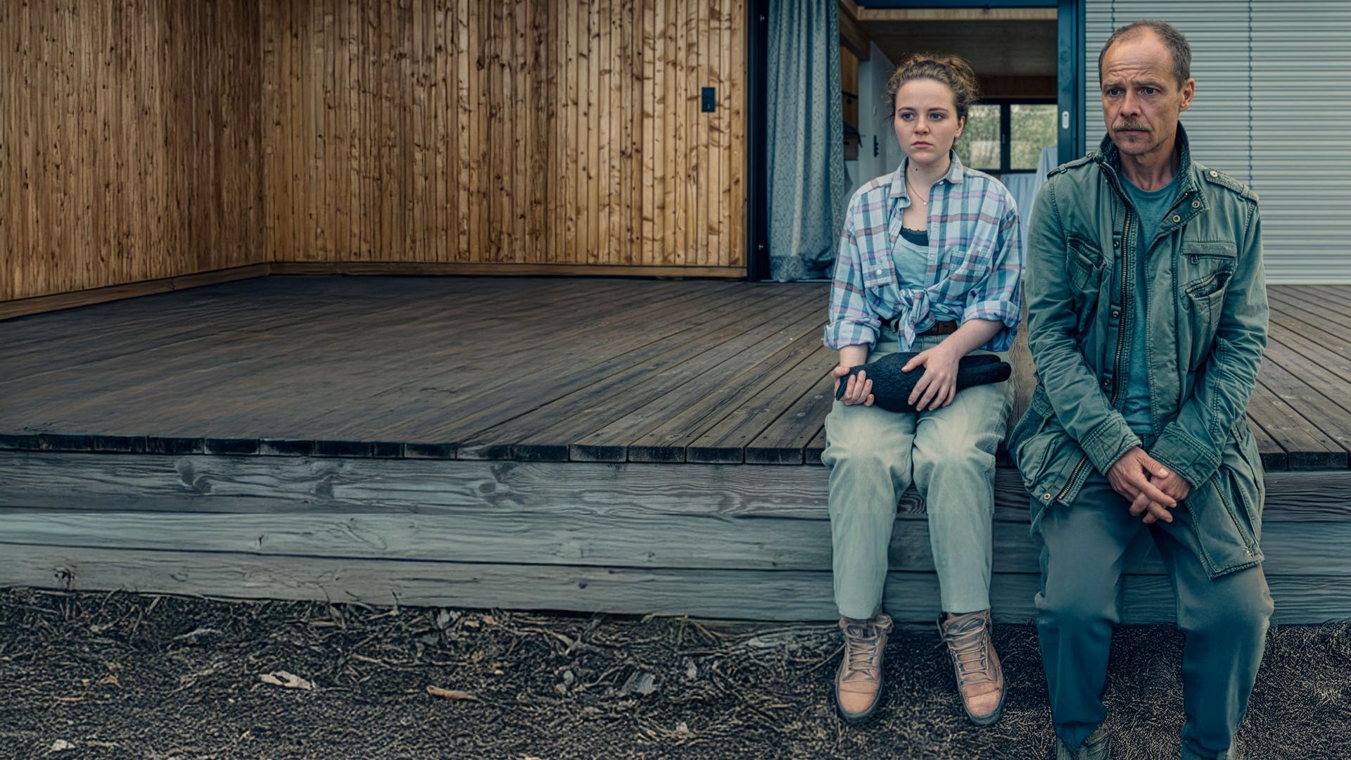 "Die Toten vom Bodensee - Das Geisterschiff": Lenka Bergdorf (Alice Prosser) und Micha Oberländer (Matthias Koeberlin) sitzen nebeneinander auf einem Bootssteg. Lenka Bergdorf hält eine Figur in der Hand.