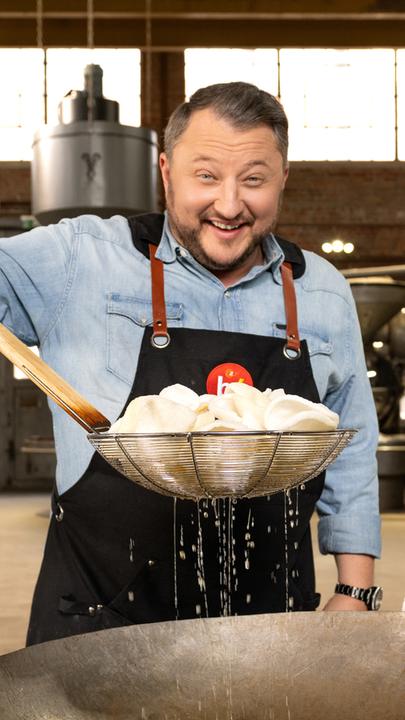 Produktentwickler Sebastian Lege hält in der rechten Hand einen Bratkorb, in dem frittierte Krabbenchips liegen. Darunter befindet sich ein Wok.