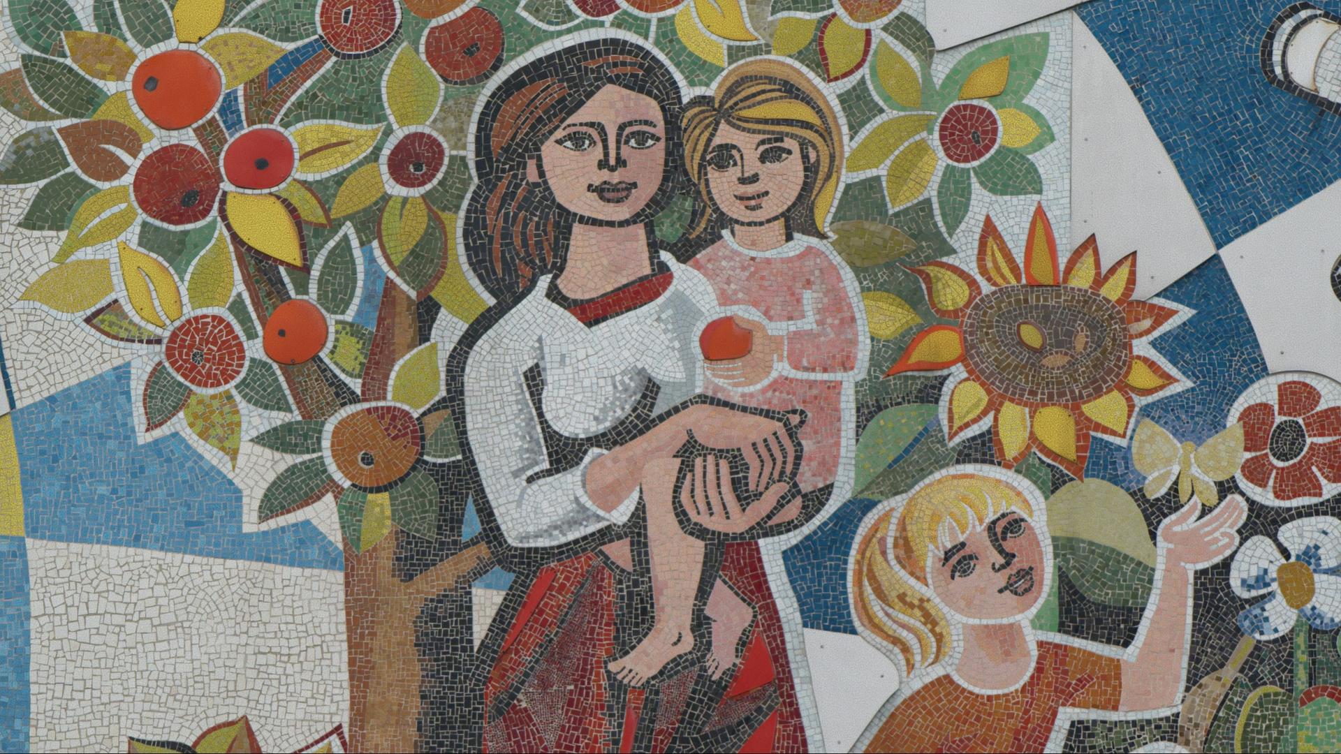 "Die Unbeugsamen 2 – Guten Morgen, ihr Schönen": Ein Teil eines Wandmosaiks. Darauf zu sehen eine Frau, die vor einem Apfelbaum ein Mädchen im Arm hält, ein Weiteres spielt mit einem Schmetterling.