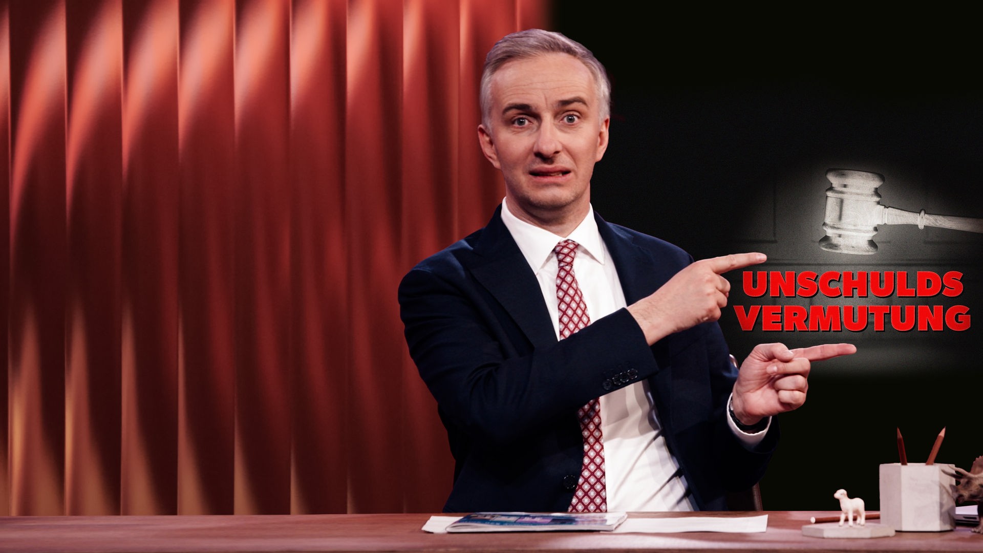 Jan Böhmermann sitzt am Schreibtisch. Rechts im Hintergrund ist ein Richterhammer abgebildet, darunter steht in roten Buchstaben: Unschuldsvermutung.