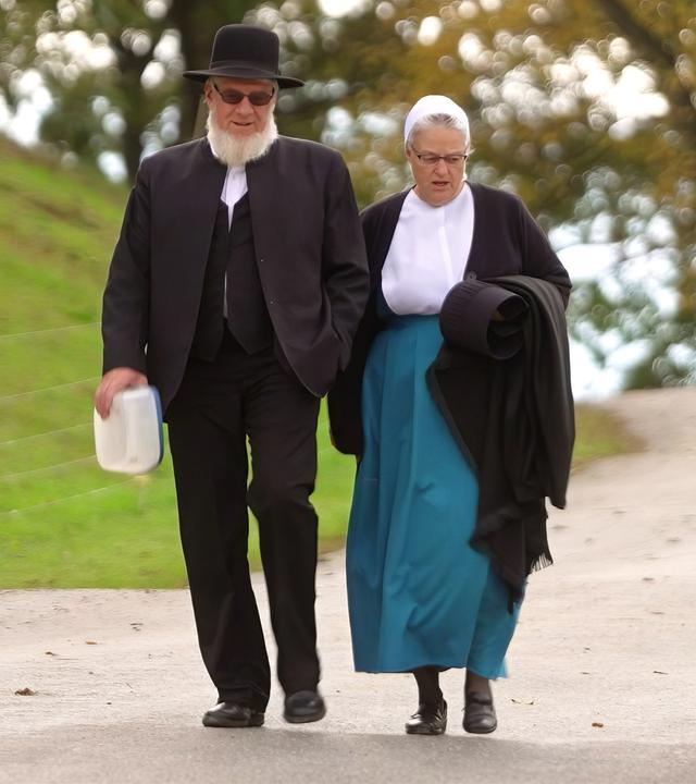 Ein älteres Paar in antiquierter Kleidung geht eine schmale Straße entlang.