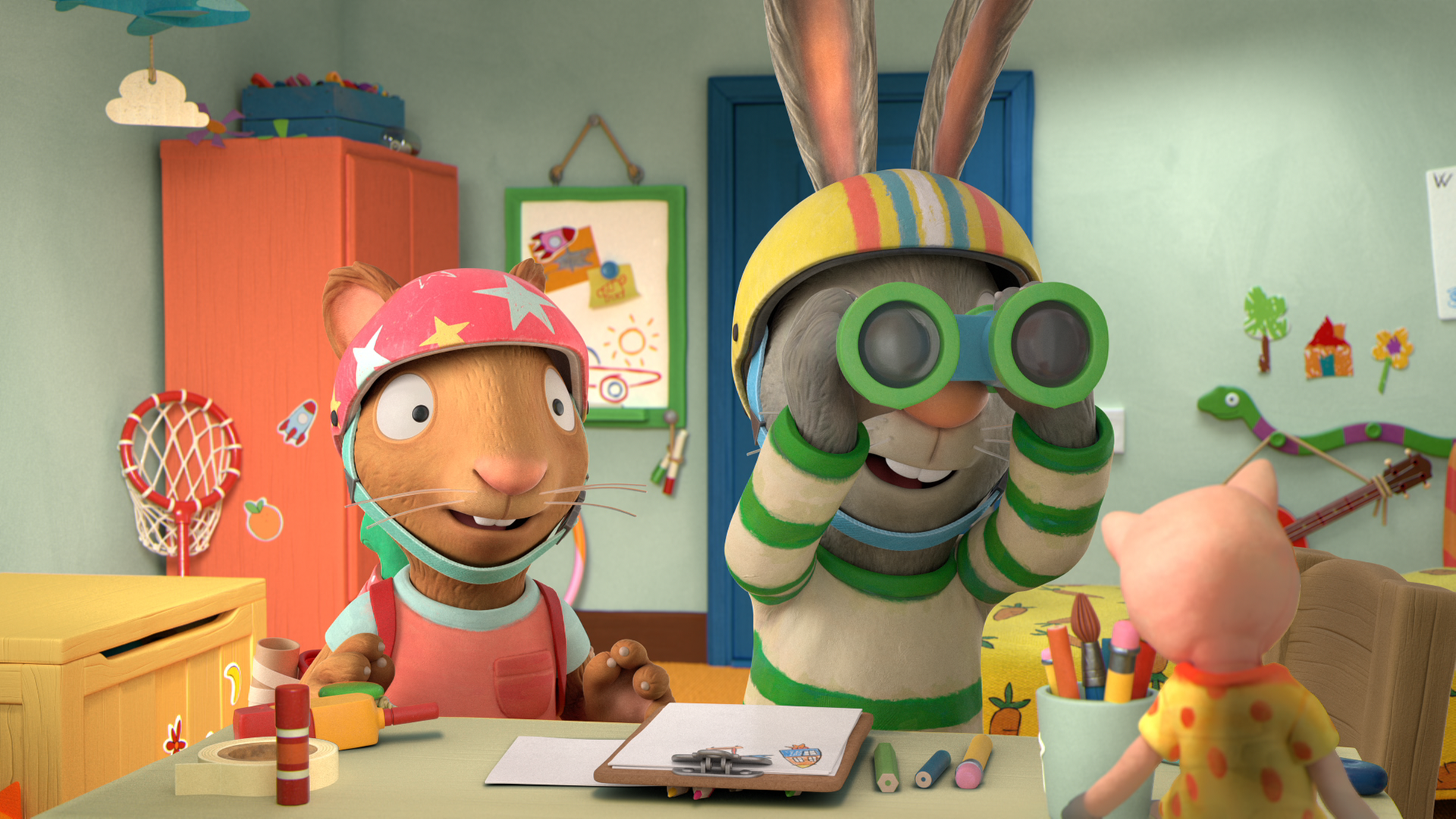 Posy und Pip tragen Helme. Pip sieht durch ein Fernglas. Auf dem Tisch vor ihnen liegen Bastelmaterialien.