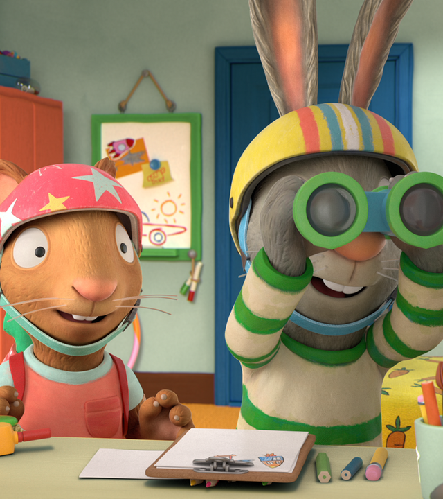Posy und Pip tragen Helme. Pip sieht durch ein Fernglas. Auf dem Tisch vor ihnen liegen Bastelmaterialien.