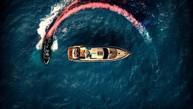 "Die Yacht": Luftaufnahme: Eine kleine, cremefarbene Yacht wird auf offener See von einem  schwarzen Motorboot umkreist. Die Spur des Motorbootes im Wasser ist rot eingefärbt, um eine Blutspur zu suggerieren.