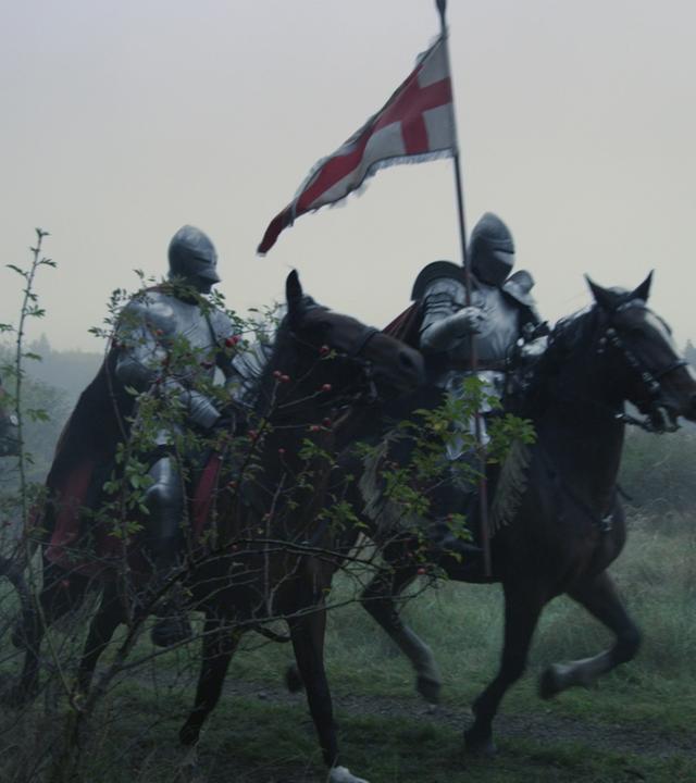 Mehrere gerüstete Ritter reiten über eine Wiese, der vorderste hält eine Fahne.
