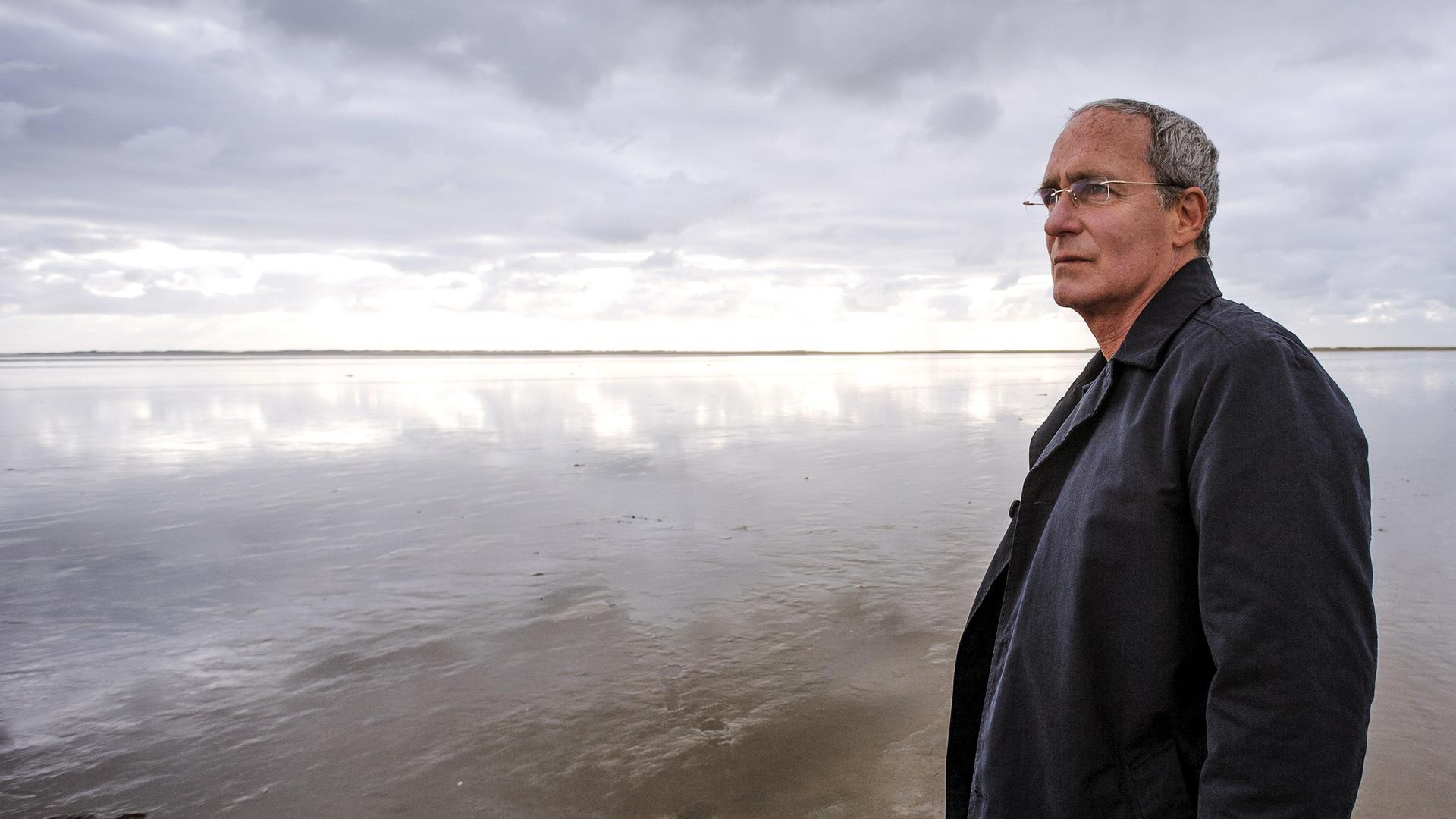 Alexander Halbach (August Zirner) steht im Watt und sieht nachdenklich aus.