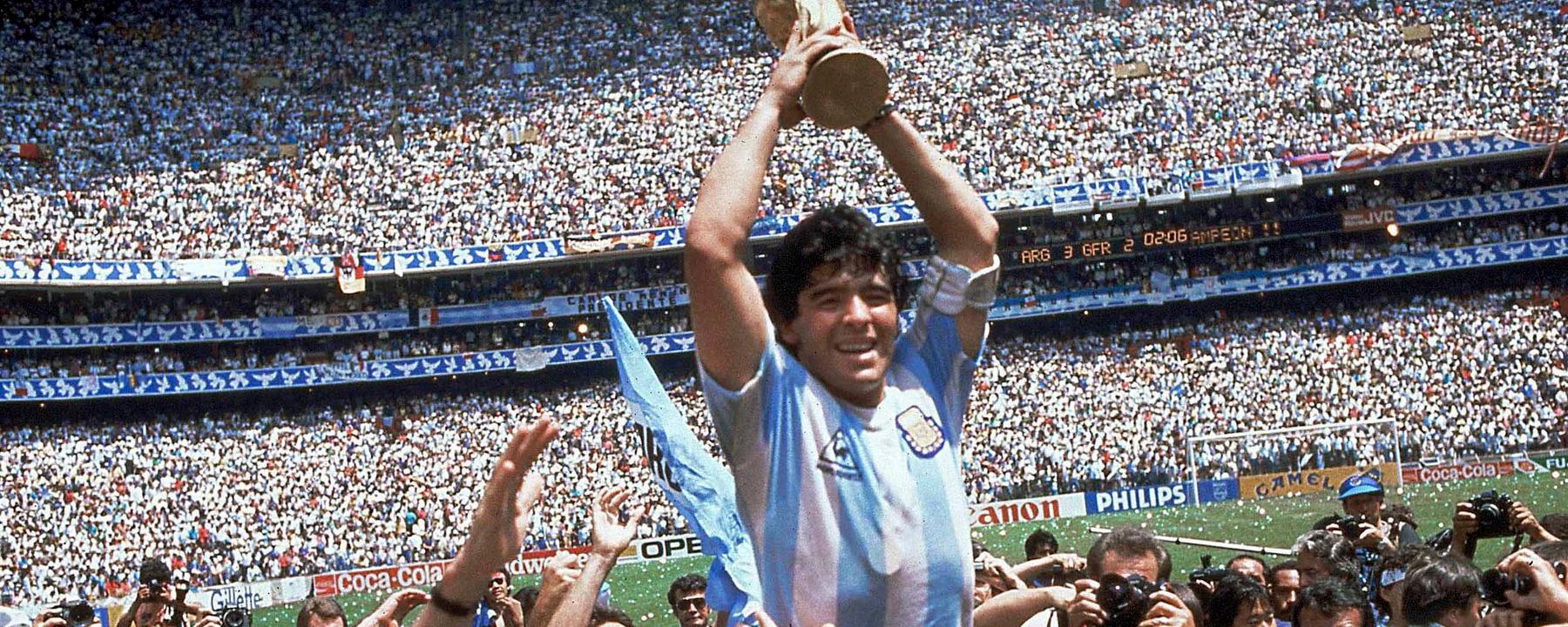 Auf dem Foto sieht man Spieler Diego Maradona, wie er von seinen Mitspielern der argentinischen Nationalmannschaft hochgehalten wird. In beiden Händen hält er den Pokal zur Fußballweltmeisterschaft über seinem Kopf.