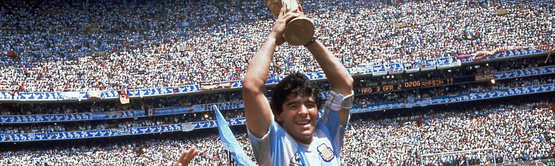 Auf dem Foto sieht man Spieler Diego Maradona, wie er von seinen Mitspielern der argentinischen Nationalmannschaft hochgehalten wird. In beiden Händen hält er den Pokal zur Fußballweltmeisterschaft über seinem Kopf.