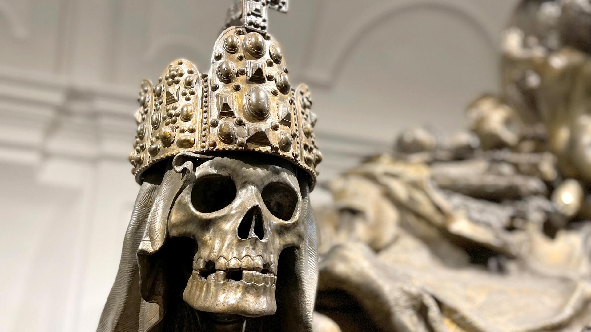 Aus Bronze gegossener Totenkopf mit Reichskrone auf einem Sarkophag