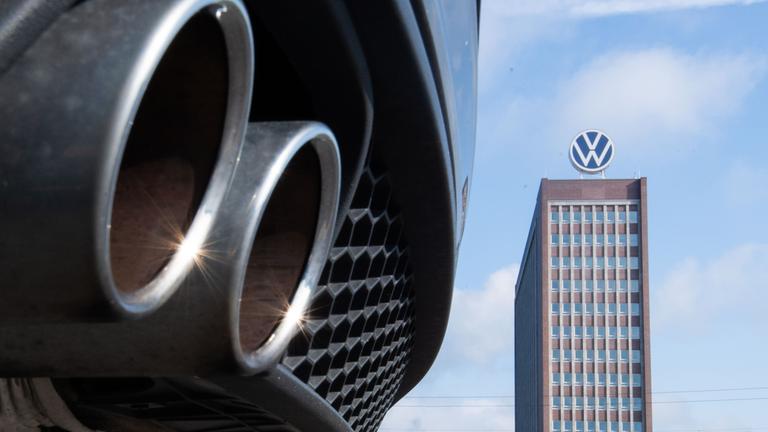Auspuffrohre eines Volkswagen, fotografiert mit dem Markenhochhaus am VW-Werk Wolfsburg im Hintergrund. (Archiv)