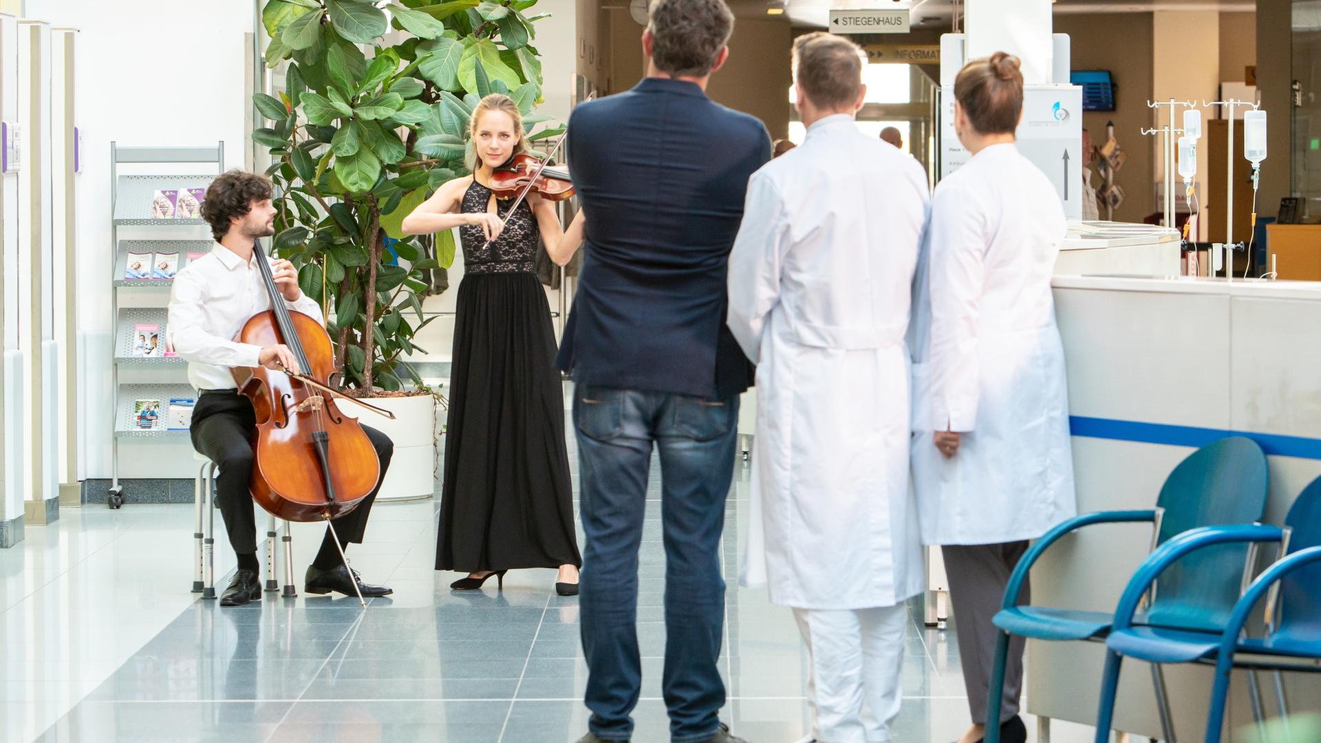 "Der Bergdoktor: Dissonanzen (2)": Steffi (Heidrun Pfeil) und Jonas (Aaron Karl) geben ein Streichkonzert in der Empfangshalle des Krankenhauses. Die Ärzte Dr. Gruber (Hans Sigl), Dr. Kahnweiler (Mark Keller) und Dr. Fendrich (Rebecca Immanuel) lauschen den Klängen.