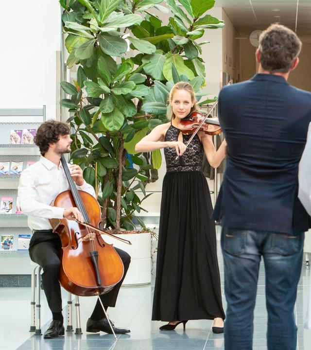 "Der Bergdoktor: Dissonanzen (2)": Steffi (Heidrun Pfeil) und Jonas (Aaron Karl) geben ein Streichkonzert in der Empfangshalle des Krankenhauses. Die Ärzte Dr. Gruber (Hans Sigl), Dr. Kahnweiler (Mark Keller) und Dr. Fendrich (Rebecca Immanuel) lauschen den Klängen.