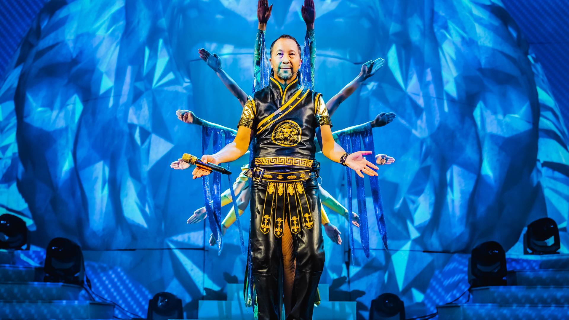 DJ Bobo vor einem blauen Bühnenbild, hinter ihm Tänzer.