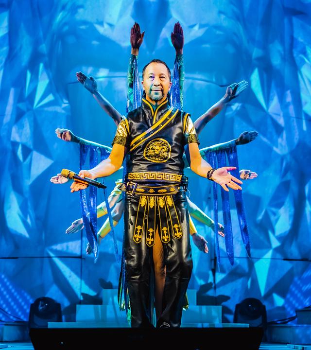 DJ Bobo vor einem blauen Bühnenbild, hinter ihm Tänzer.
