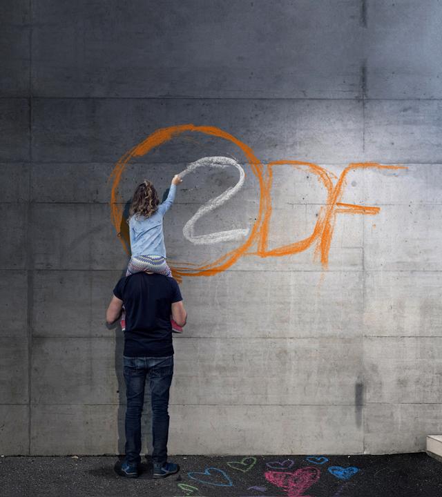Typical für Bereich Strategie der ZDF-Entsprechenserklärung: Mädchen auf Schultern von Mann malt das ZDF-Logo auf eine graue Wand