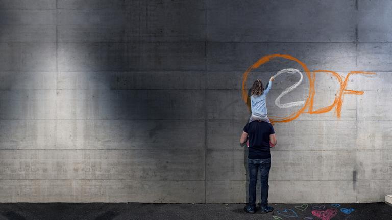Typical für Bereich Strategie der ZDF-Entsprechenserklärung: Mädchen auf Schultern von Mann malt das ZDF-Logo auf eine graue Wand