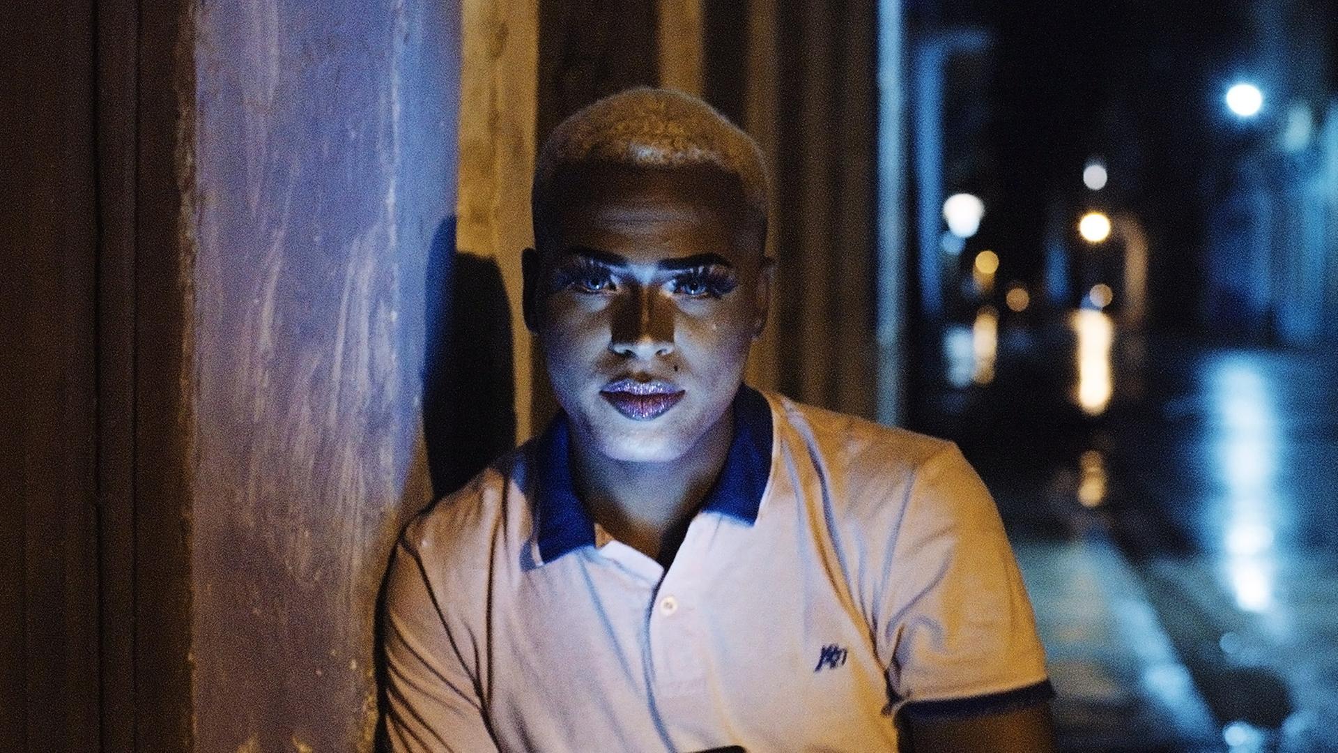 Portraitbild eines schönen jungen Mannes mit kurzrasierten, blond gefärbten Haaren und geschminktem Gesicht.