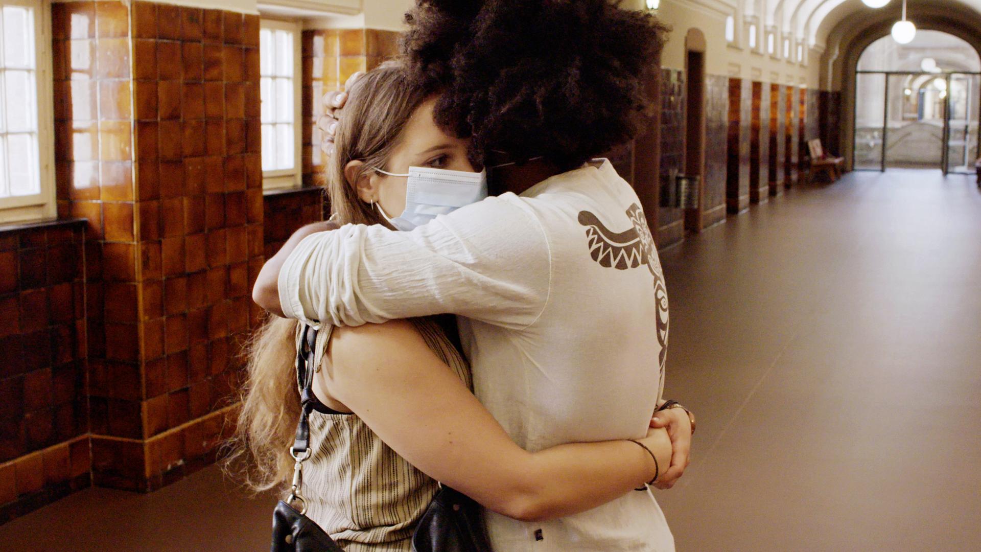 Zwei Personen stehen auf einem langen Flur und umarmen sich.