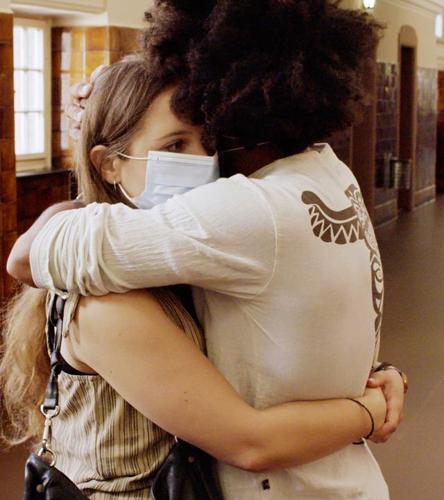 Zwei Personen stehen auf einem langen Flur und umarmen sich.