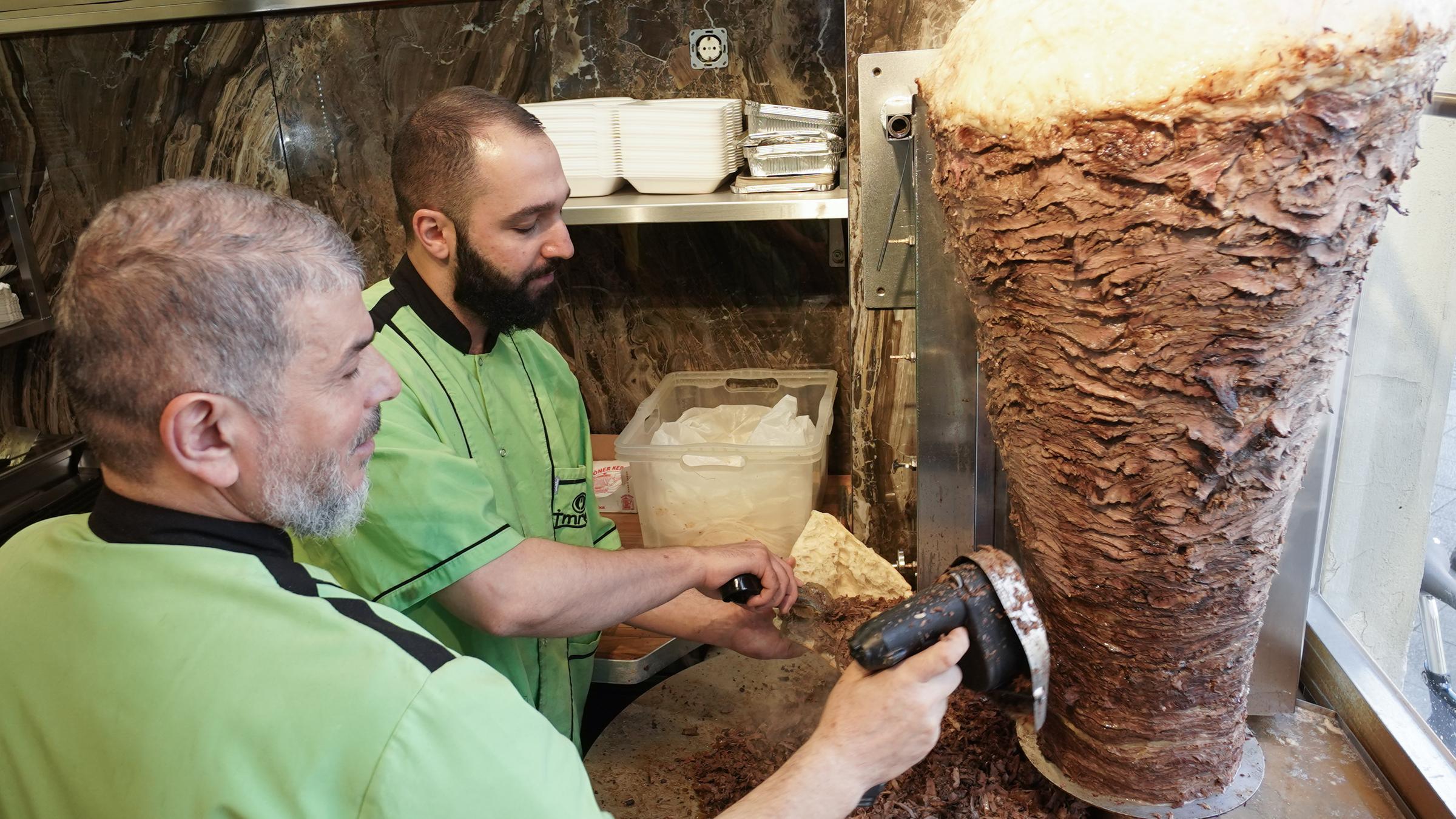 Halit (l) und Halip vom Imren Grill bereiten einen Döner zu.