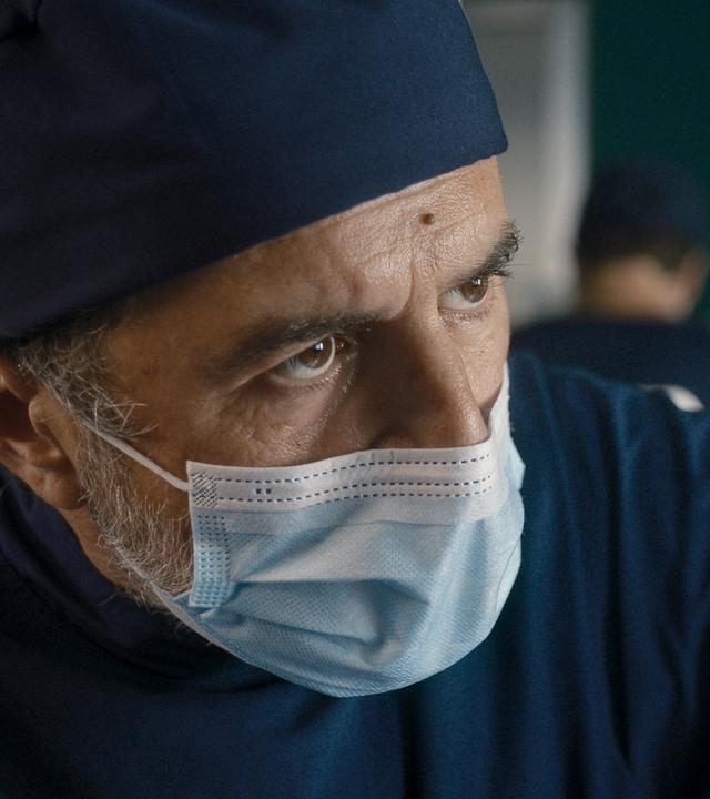 "Doktor Ballouz - Leere Seiten": Großaufnahme von Doktor Ballouz (Merab Ninidze). Er trägt OP-Kleidung sowie einen Mundschutz. Er schaut ganz konzentriert während des Eingriffes.