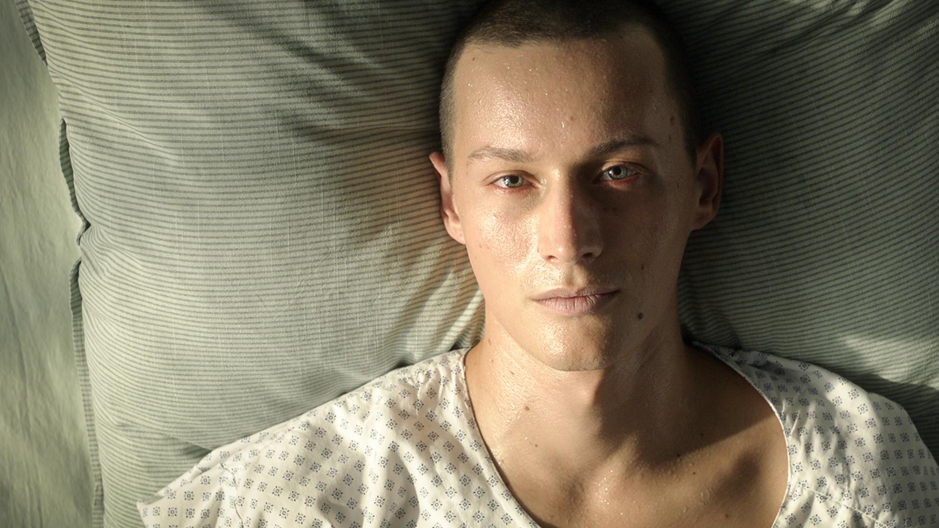Matti liegt im Krankenbett und wartet auf die rettende Knochenmarkspende. Sein Gesicht ist sehr blass und von Schweißperlen überzogen.