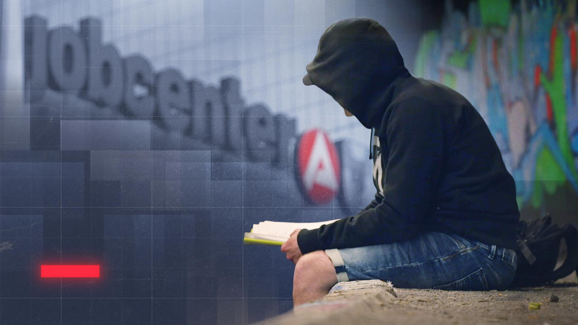 Mann mit schwarzem Hoodie sitzt vor einem Gebäude mit "jobcenter"-Schriftzug