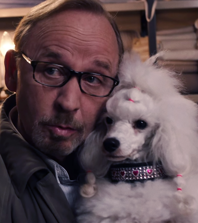Ludwig Schaller (Alexander Held) hält einen weißen Schoßhund und zieht eine Schnute. 