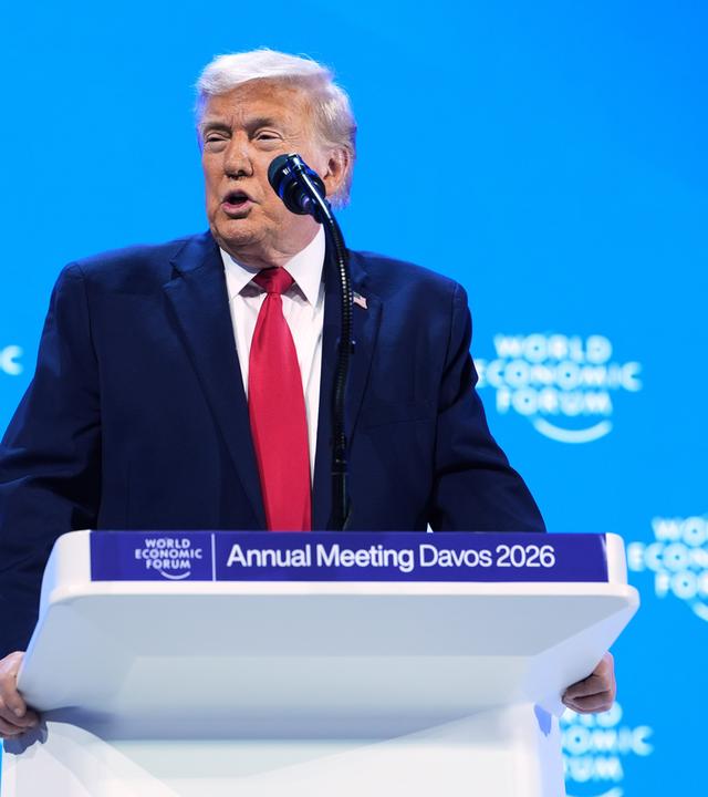 Ein älterer Mann im dunklen Anzug mit roter Krawatte spricht in ein Mikrofon.