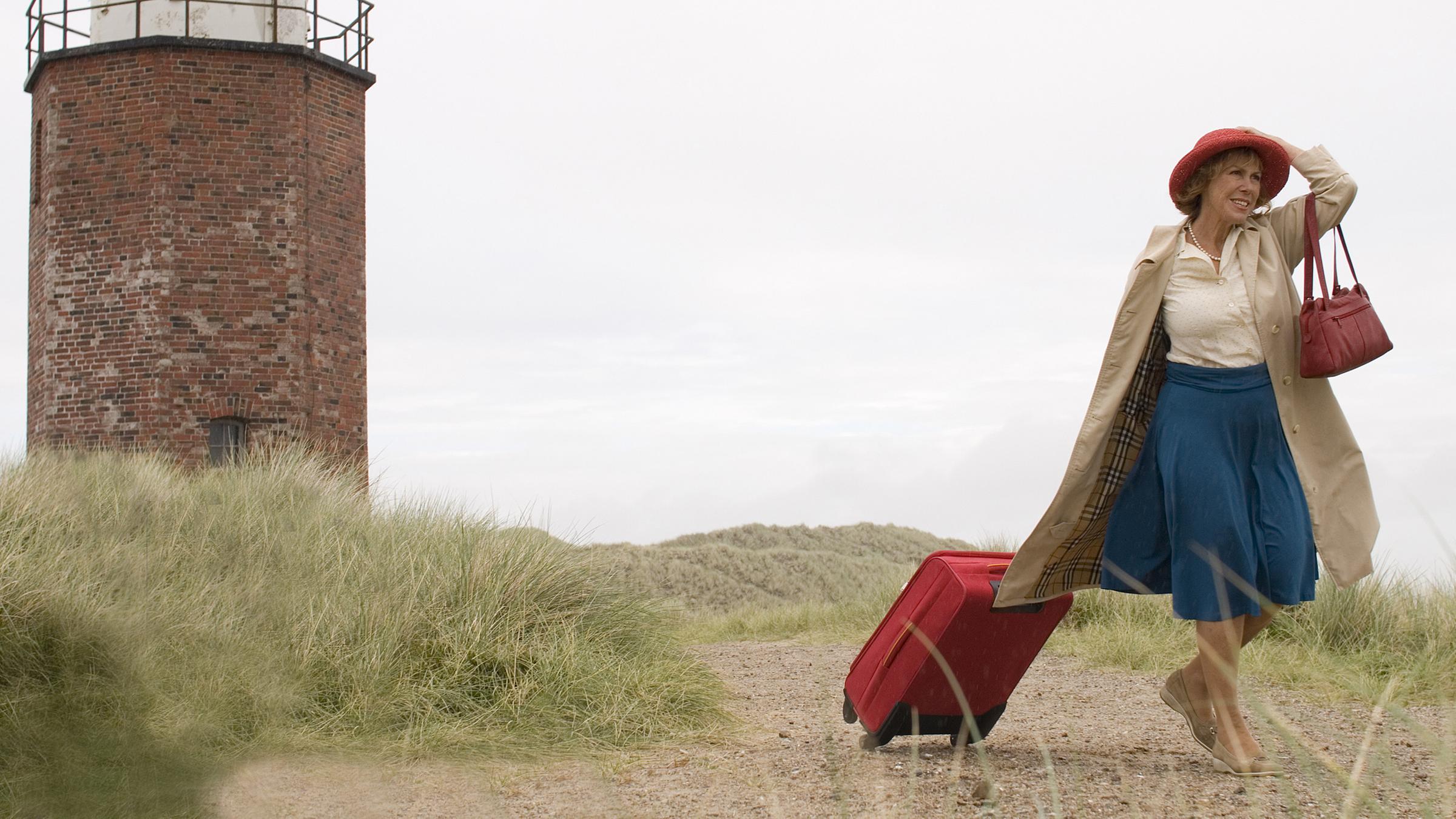Auf der Insel Sylt läuft Inge (Gaby Dohm) an einem Leuchtturm vorbei. Sie zieht mit der rechten Hand einen Koffer hinter sich her und hält mit der anderen Hand ihren Hut auf dem Kopf fest.