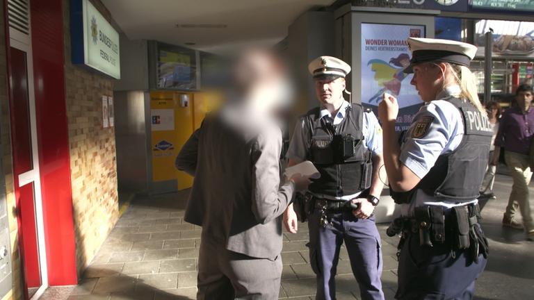 "Dorfpolizist und Großstadt-Cop - Ordnungshüter im Einsatz": Eine Polizistin und ein Polizist im Gespräch mit einem Mann. Sie stehen vor dem Münchner Hauptbahnhof.