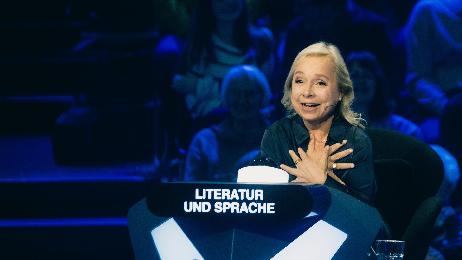 "Der Quiz-Champion": ChrisTine Urspruch sitzt am Ratepult im Studio und gestikuliert.