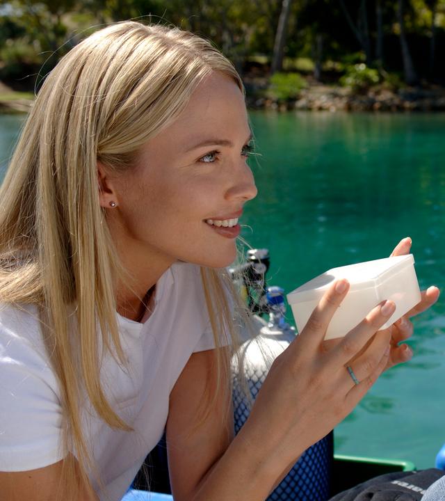 Lewis unterhält sich mit der Meeresbiologin. Lewis (rechts) trägt einen beigefarbenen Fischerhut und schaut die Meeresbiologin (links) an, die eine weiße kleine Schachtel in der Hand hält und ihn anlächelt.