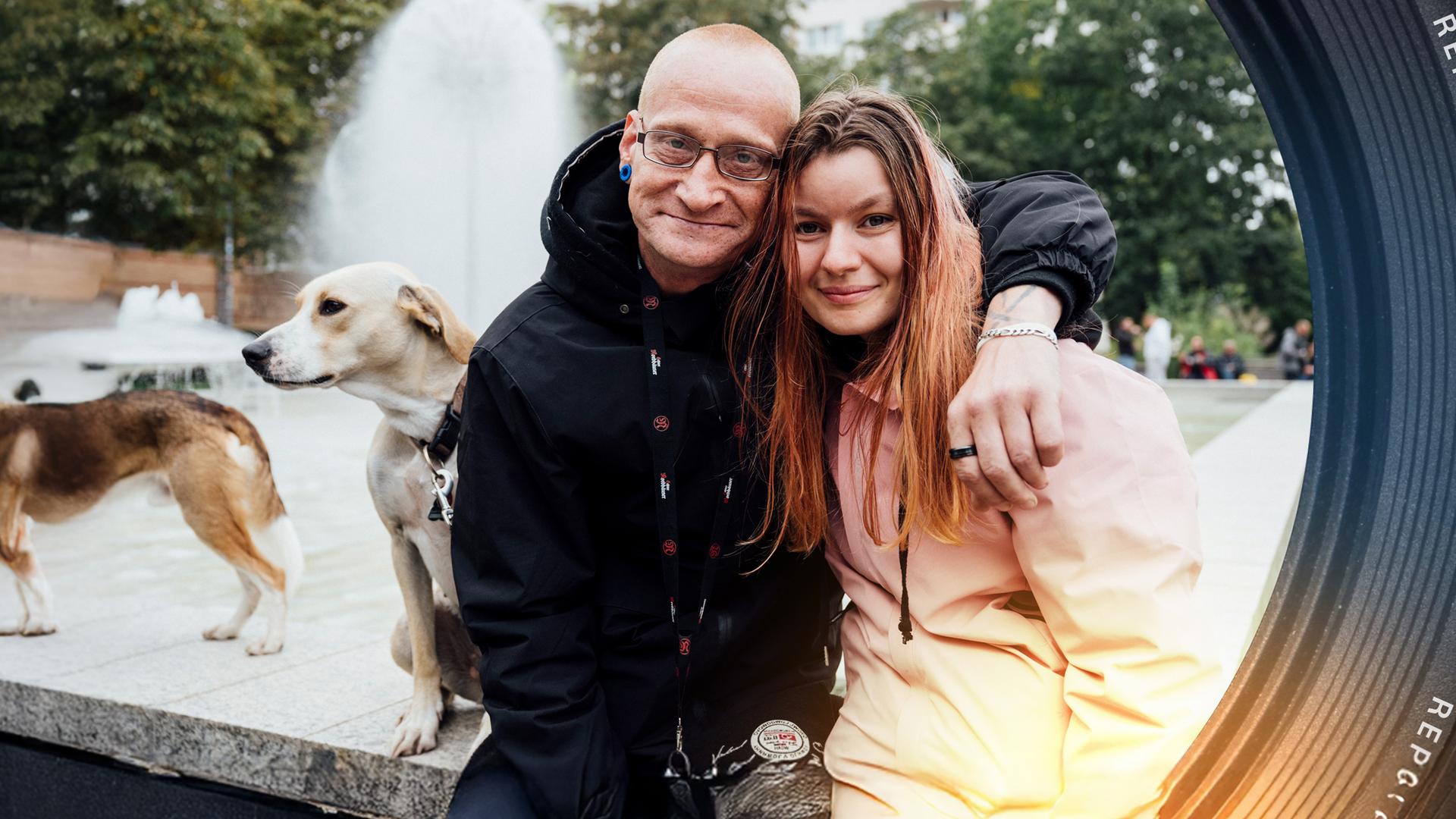 Vor einem Springbrunnen: Ein Mann, "Monte", hat den Arm um die Schulter seiner Freundin gelegt. Neben ihnen sitzt ein Hund.