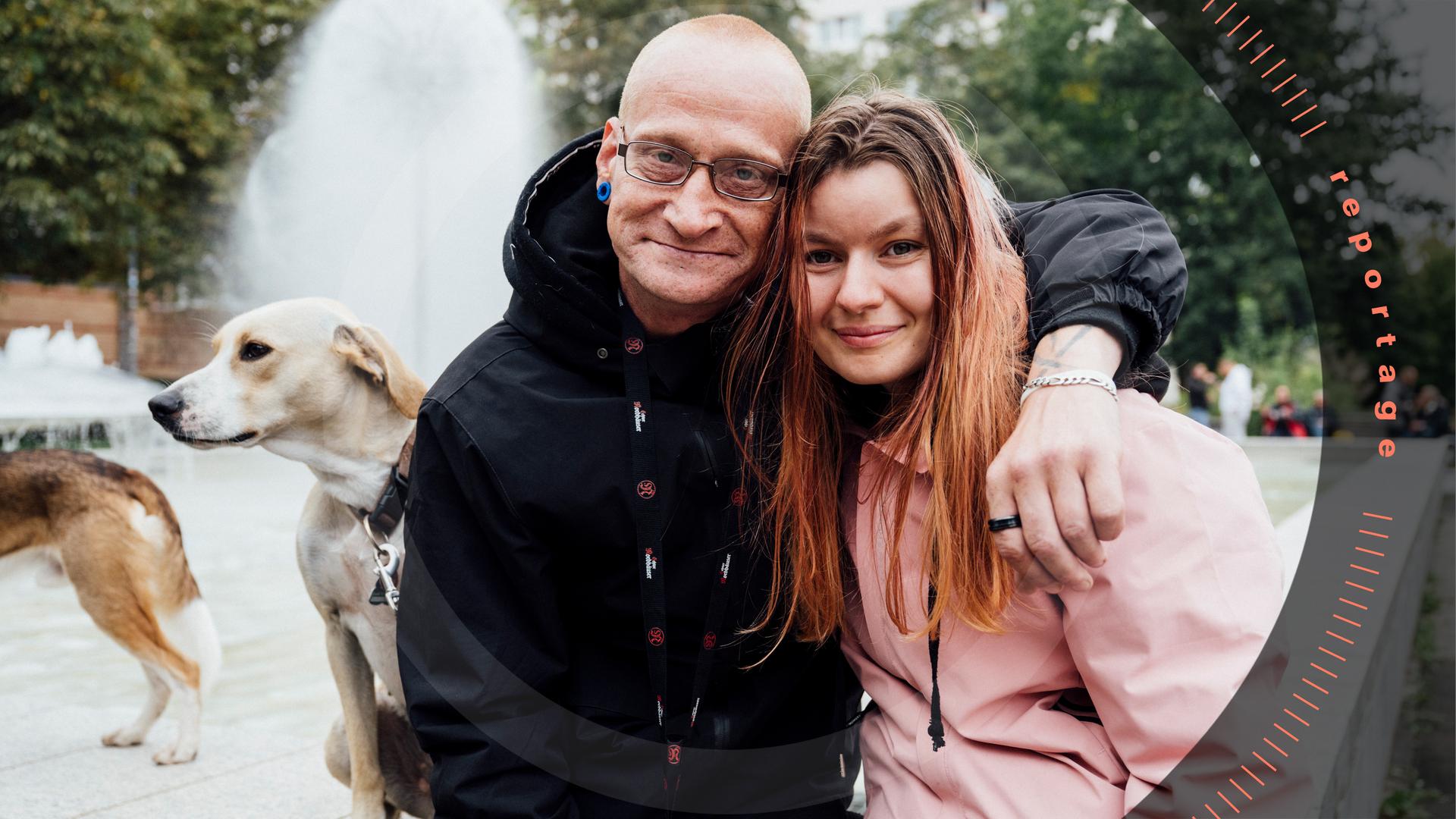 Vor einem Springbrunnen: Ein Mann, "Monte", hat den Arm um die Schulter seiner Freundin gelegt. Neben ihnen sitzt ein Hund.