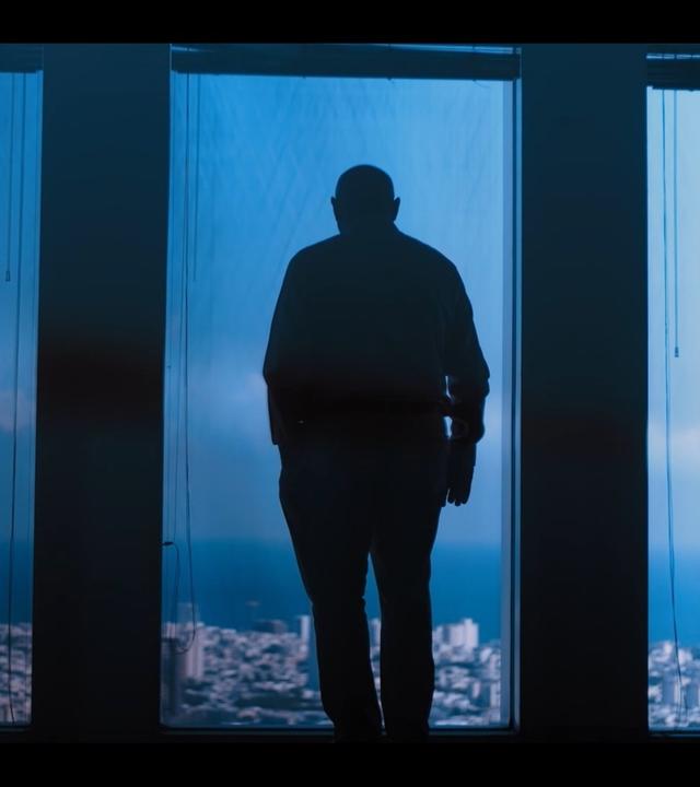 Udi Levi steht mit dem Rücken zur Kamera vor einem großen Fenster und blickt auf Tel Aviv hinab.