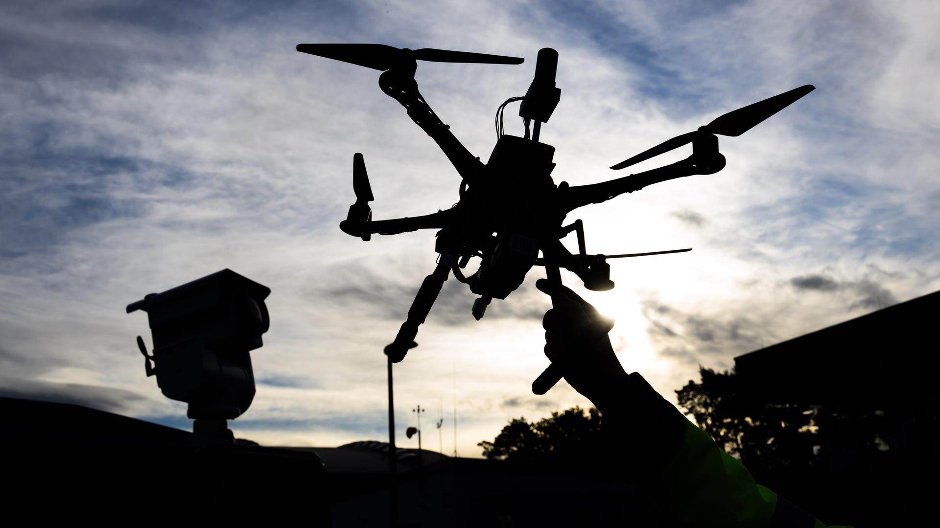 Der dunkle Umriss einer Drohne, die von einer Hand vor einen bewölkten Himmel hochgehalten wird.
