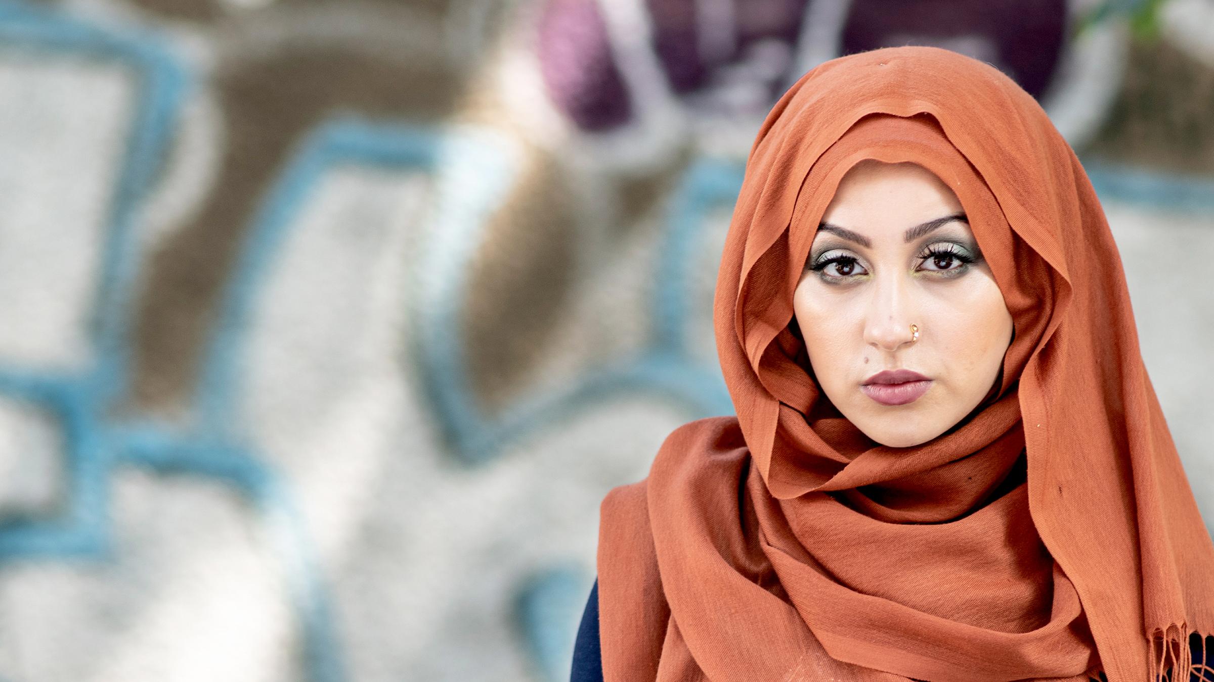 Amira (Tua El-Fawwal) steht vor einer Mauer mit Graffiti und schaut in die Kamera (Großaufnahme).