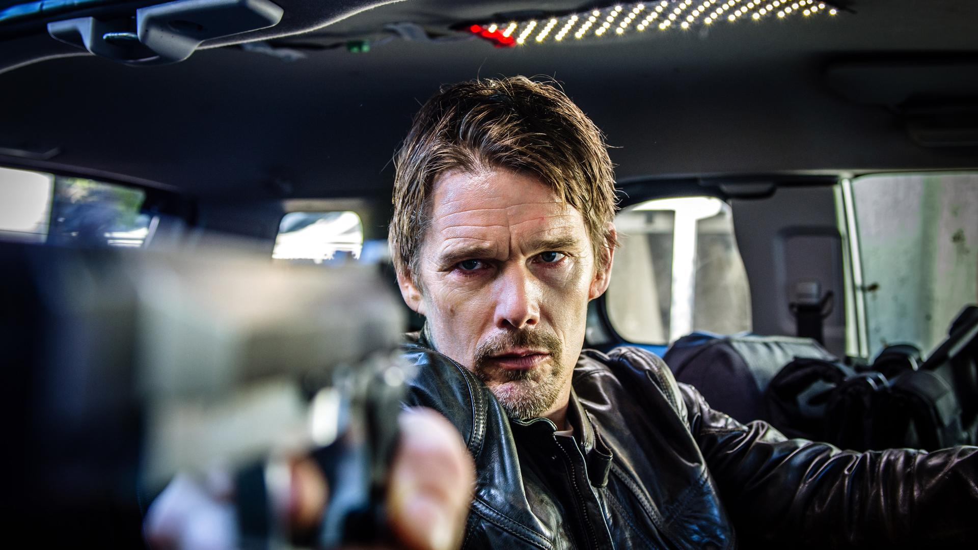 Travis Conrad (Ethan Hawke) sitzt in einem Auto und zielt mit einer Pistole aus dem Seitenfenster.
