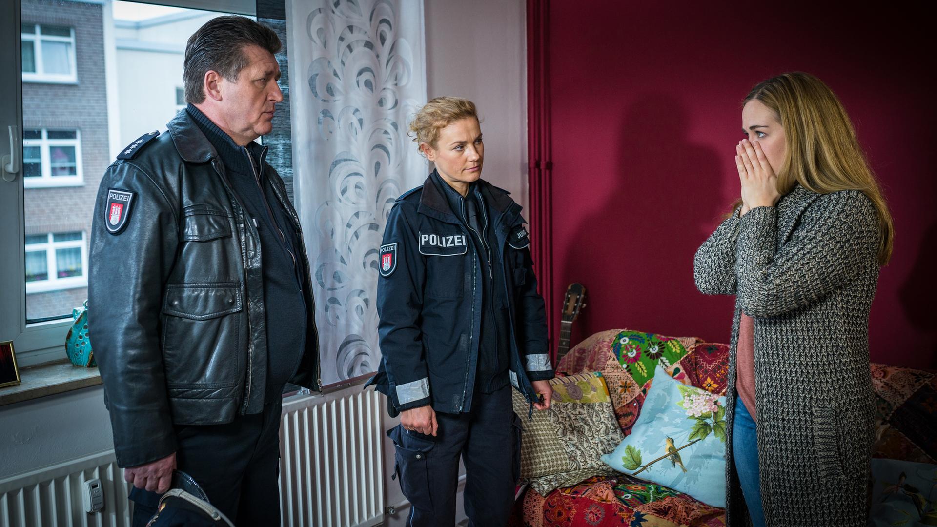 Verena Riwa (Annina Hellenthal, r.) ist außer sich. Sie erzählt Hans (Bruno F. Apitz, l.) und Franzi (Rhea Harder-Vennewald, M.), dass ihr Stalker Roman Goldt in ihre Wohnung eingebrochen sein muss, um ihr einen Strauß roter Rosen hinzustellen.