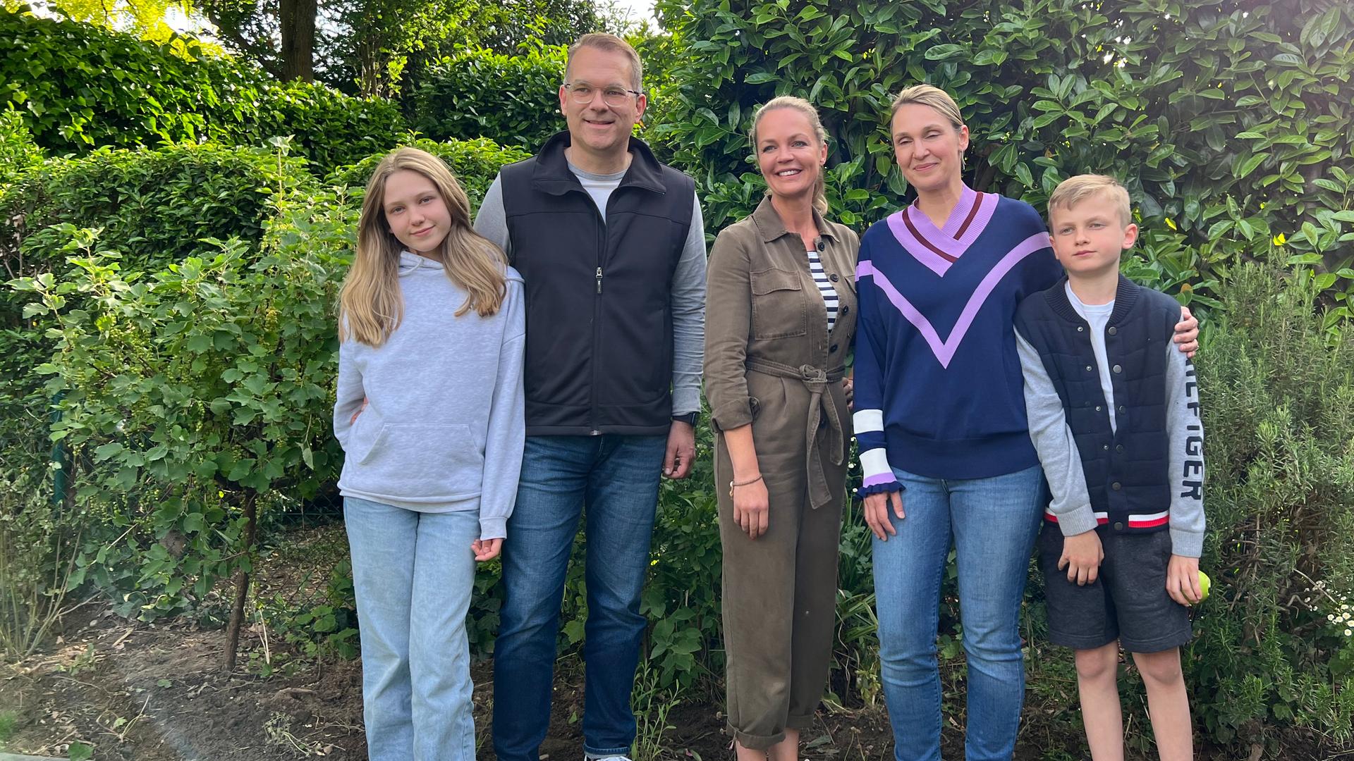 Familie Kossey stehen mit Eva Brenner vor einer Hecke und lächeln in die Kamera.